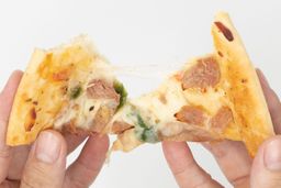 Two hands break apart a slice of pizza with cheese, meat, onions, and green bell peppers on top baked using a toaster oven.