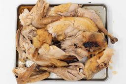 Eight pieces of a carved chicken including two carcass halves, two breasts, two wings, and two thighs on a baking pan.