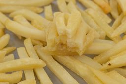 Eight pieces of broken-up baked french fries are stacked on top of pieces of whole fries on a silver baking pan.