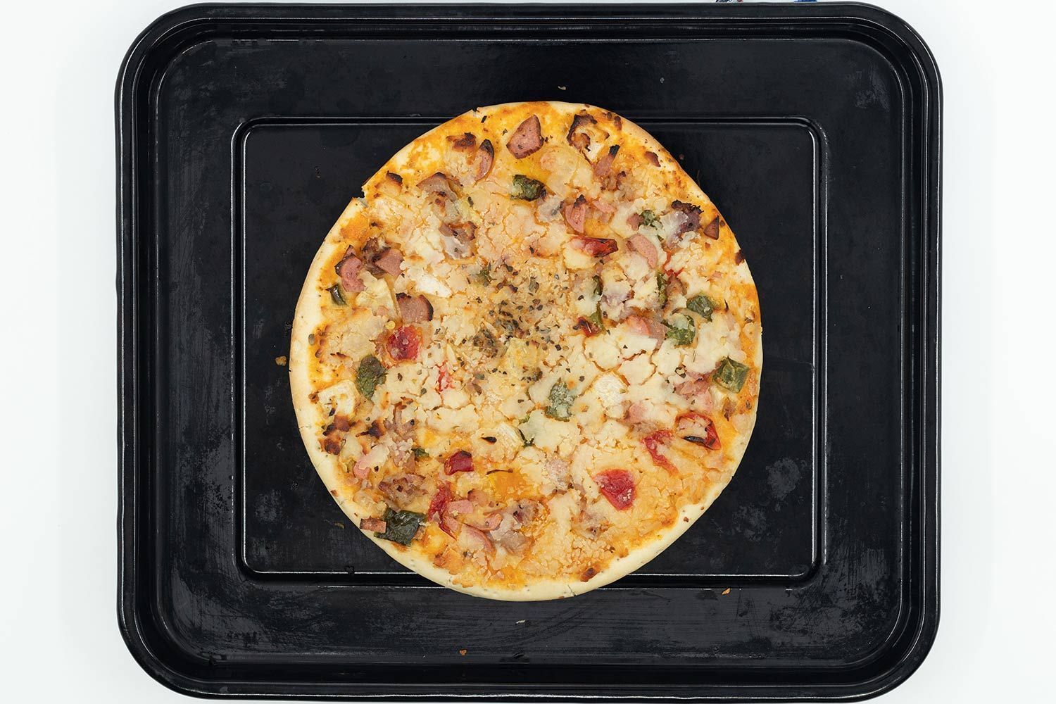 Ninja Foodi XL Pro Air Toaster Oven PizzaA toaster oven baked 9-inch thick-crust meat pizza with cheese, onions, and green bell peppers on top inside a baking pan.