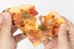 Two hands break apart a slice of pizza with cheese, meat, onions, and green bell peppers on top baked using a toaster oven.