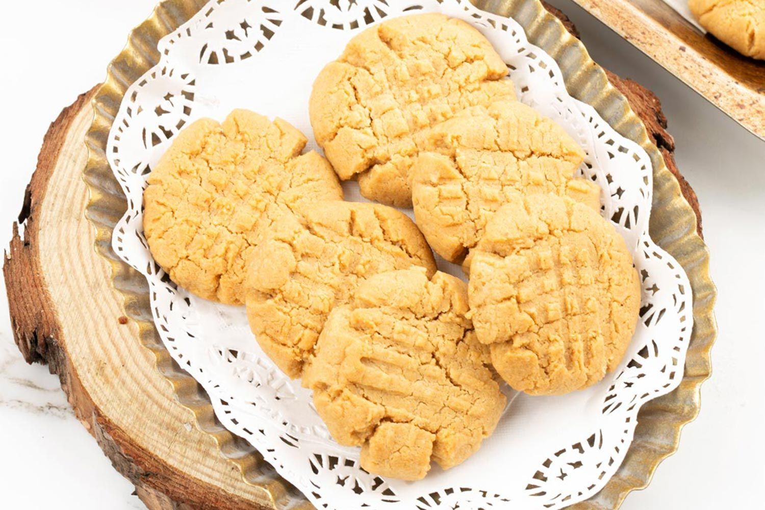 Six golden cookies on top of a paper lining in a serrated dish on top of a wooden tray resembling the cross surface of a log.