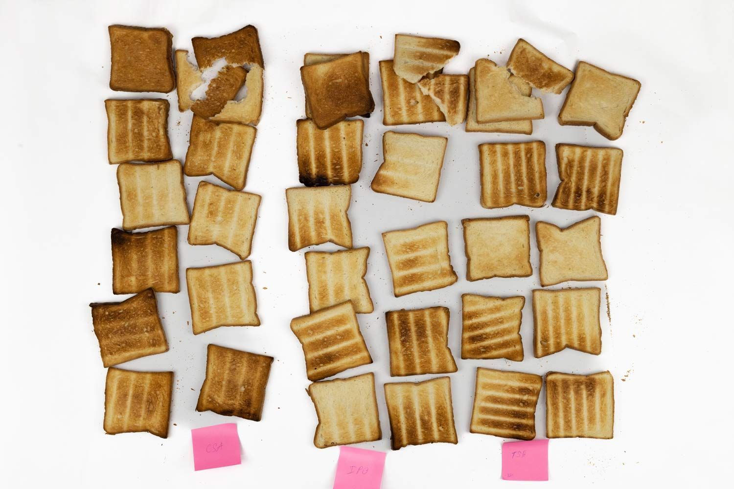 On a white background, 35 pieces of toast with four pieces broken in halves and 3 pink stickers with toaster ovens’ names.