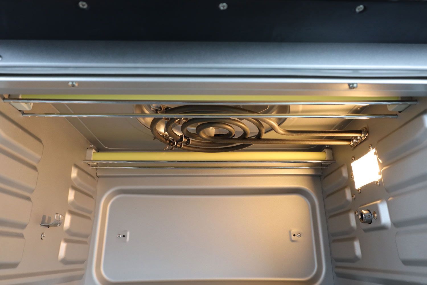 The cooking chamber of the Instant Omni Plus 18L Toaster Oven has two quartz and one swirl nichrome heating element, four rack levels, a rotisserie socket and bracket, and a shining light on the right.