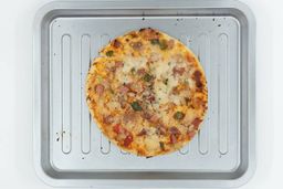 A toaster oven baked 9-inch thick-crust meat pizza with cheese, onions, and green bell peppers on top. The pizza is inside a grooved silver baking pan on a white background.