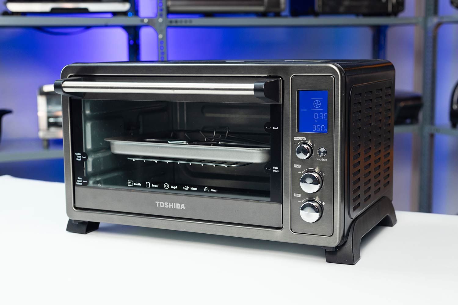 The front of a closed Toshiba AC25CEW-BS Convection Toaster Oven has a control panel and a glass door with a handle.