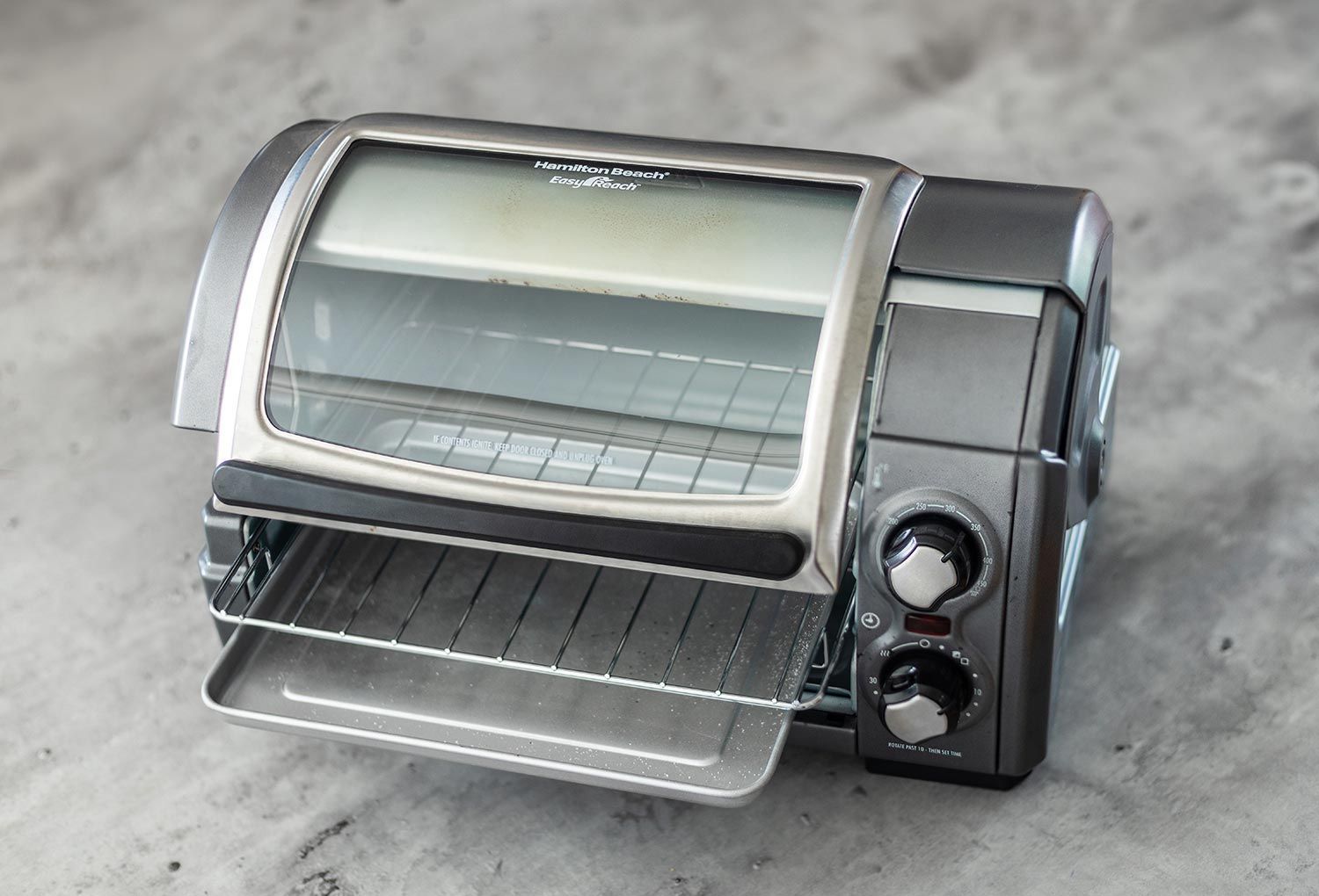 The front of a closed stainless steel Hamilton Beach 31127D 6-Slice Easy Reach Roll Top Toaster Oven on a white background.