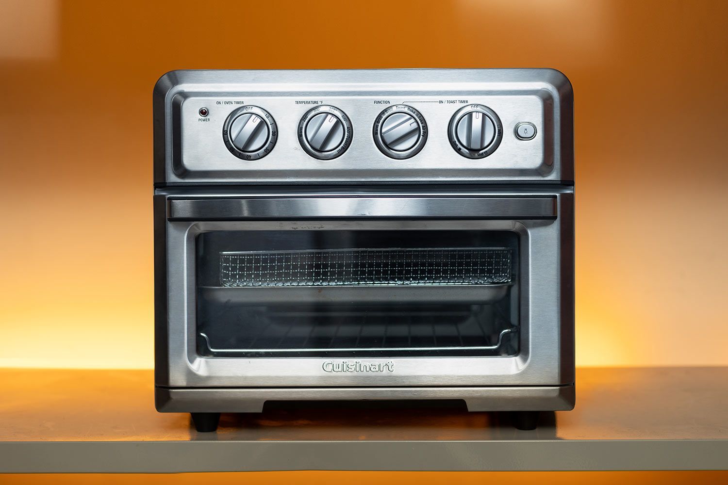 The front of a closed Cuisinart TOA-60 Convection Toaster Oven Air Fryer. The control panel is positioned horizontally on the upper front. Below the control panel is the door handle. The glass door is covered with an illustration.