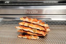 A close-up of 5 slices of pizza stacked on top of each other inside an air-fryer basket in front of the Breville BOV900BSS Smart Oven Air Fryer Pro.