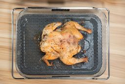 The backside of a whole roasted chicken inside an air-fryer basket on top of a baking pan.