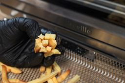 A close-up of a hand holding pieces of broken fries. In the background is a basket of air-fried fries and the Breville BOV900BSS Smart Oven Air Fryer Pro on a wooden table.