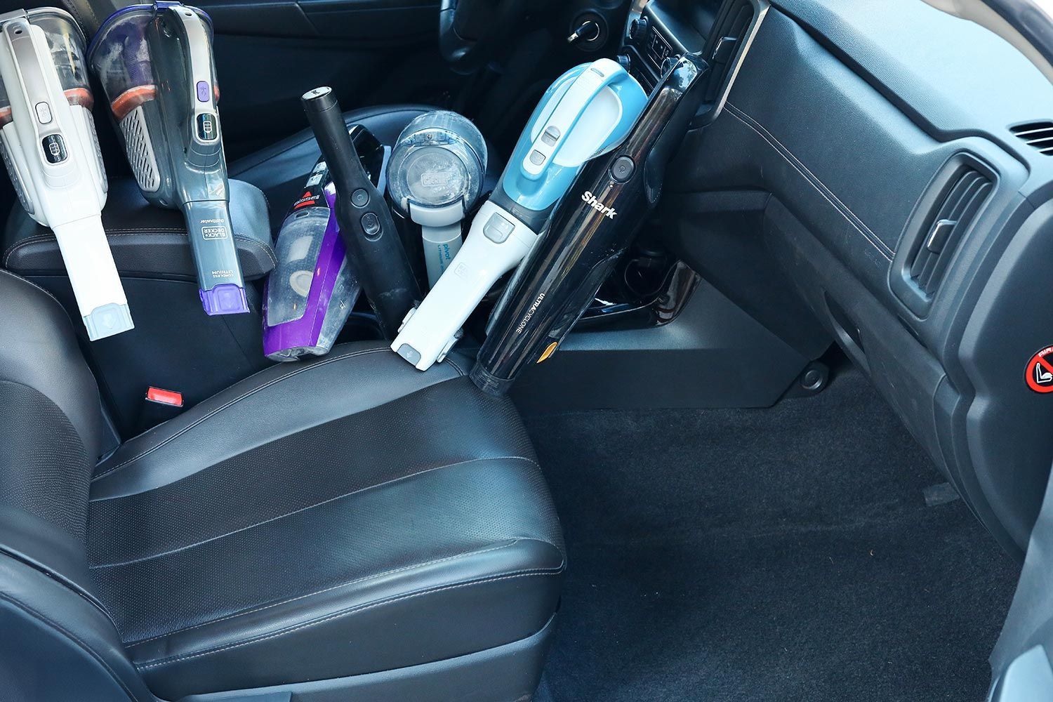 A selection of handheld vacuum cleaners lined up in a car interior, ready for a side-by-side performance comparison test.