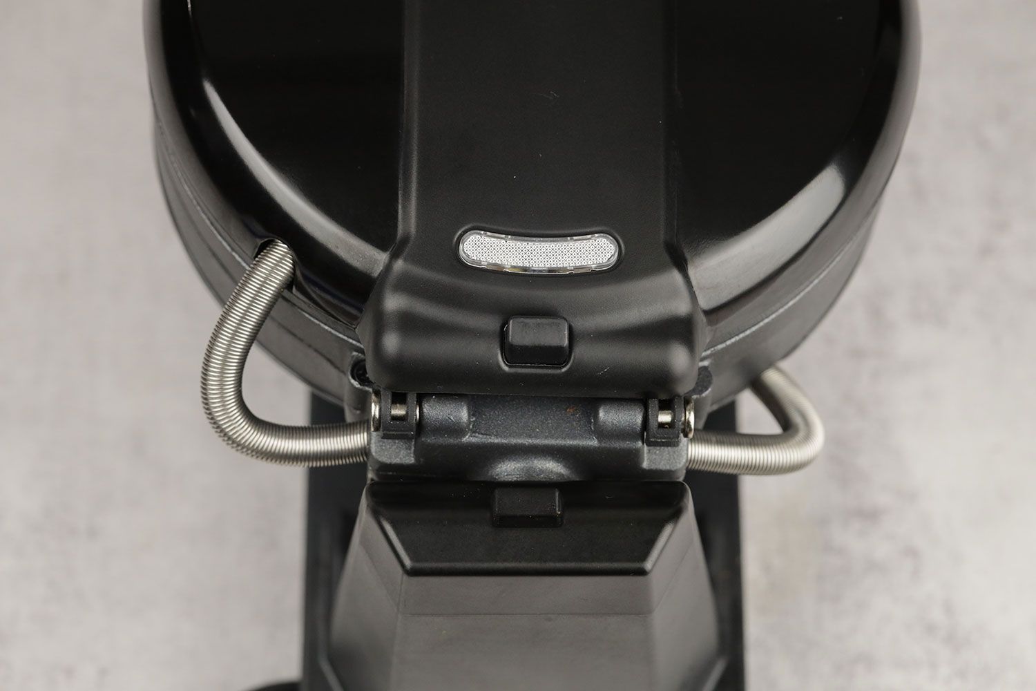 The back hinge of the Black and Decker WMD200B rotating waffle maker’s baking chamber. Two metallic cabling sleeves are snaking around the back.