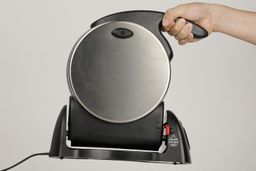 The entire Presto waffle maker is held in the air by the handle with one hand of a product tester.