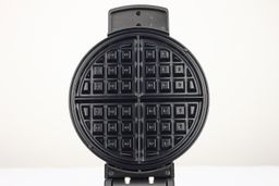 A close-up view of the glossy, black, Belgian-style waffle plate of the Black and Decker WMB500 waffle maker.