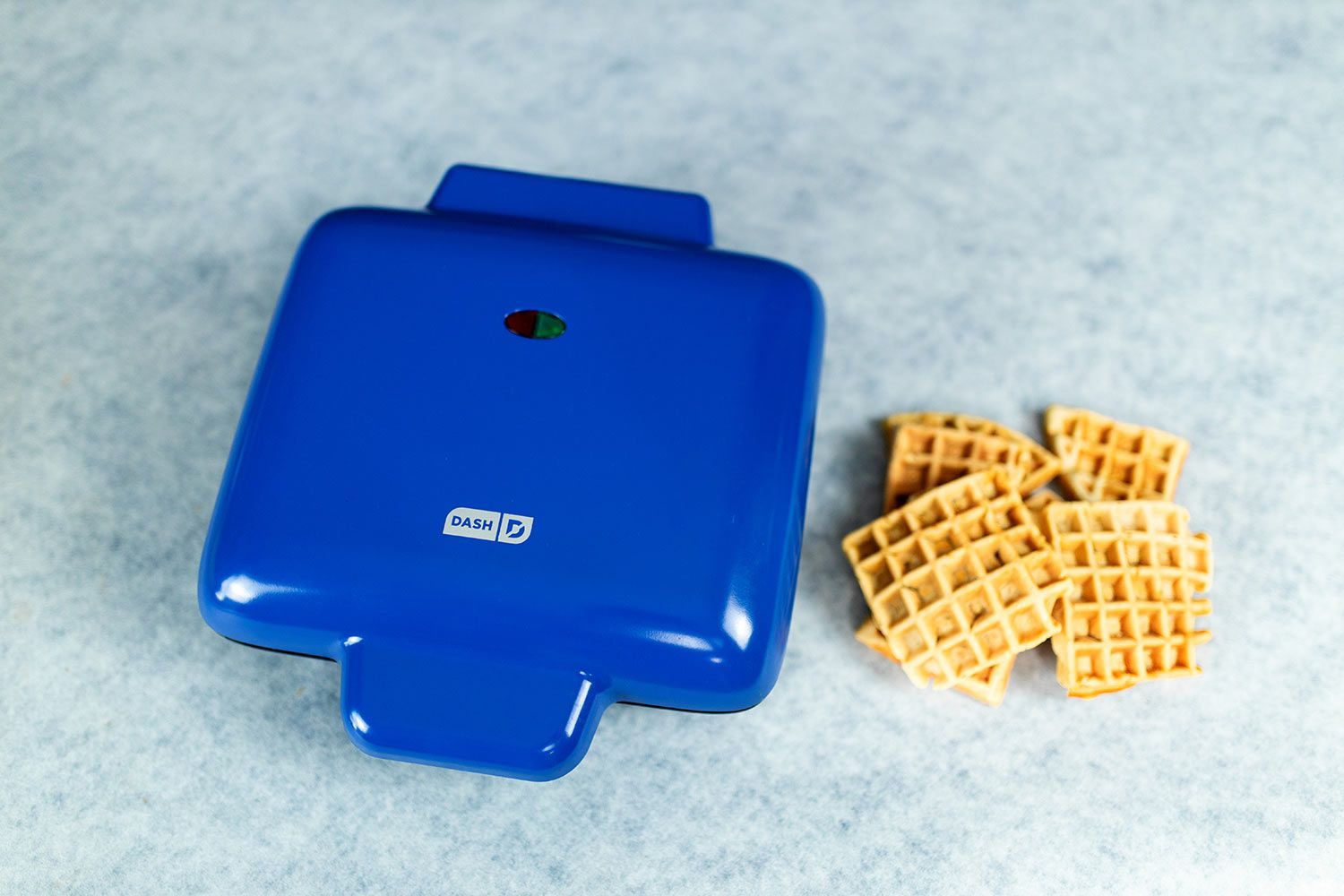 DASH No-Drip Waffle Maker next to a pile of fresh golden waffles.