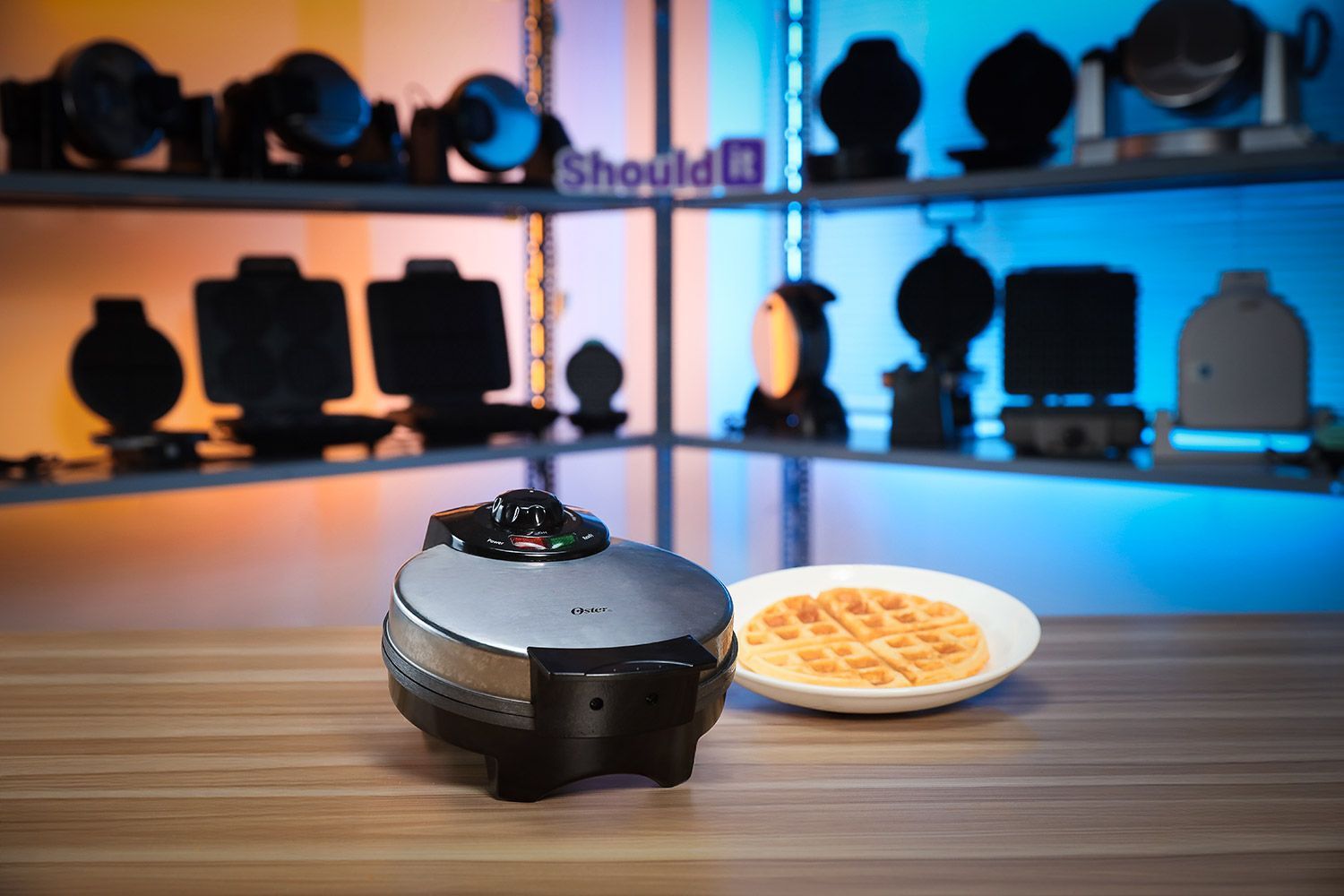 The Oster waffle maker on a wooden floor next to a plate of 7-inch and mini waffle makers.