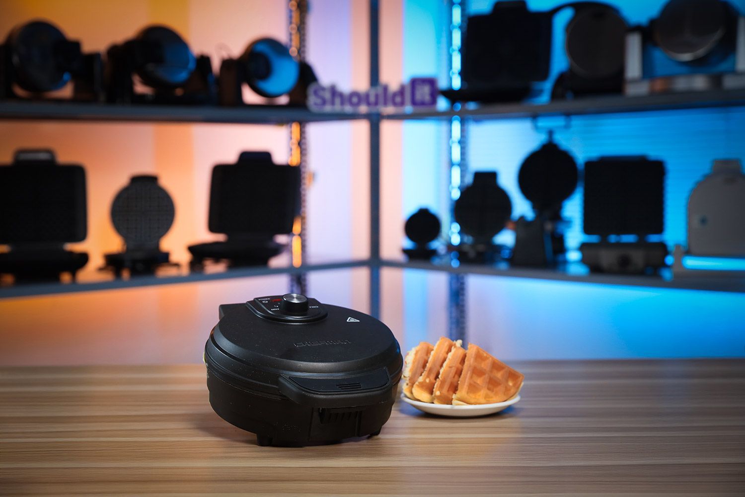 Chefman Anti-Overflow waffle maker with empty waffle plates on a white tabletop next to a plate containing stacks of waffles.