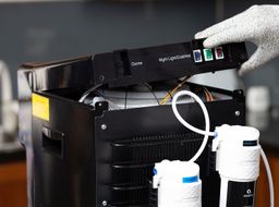 A gloved hand lifting the unscrewed top off a water cooler dispenser partly revealing the tank and wiring inside.