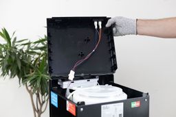 The opened hood of a water cooler dispenser with wires attached to an installation point.