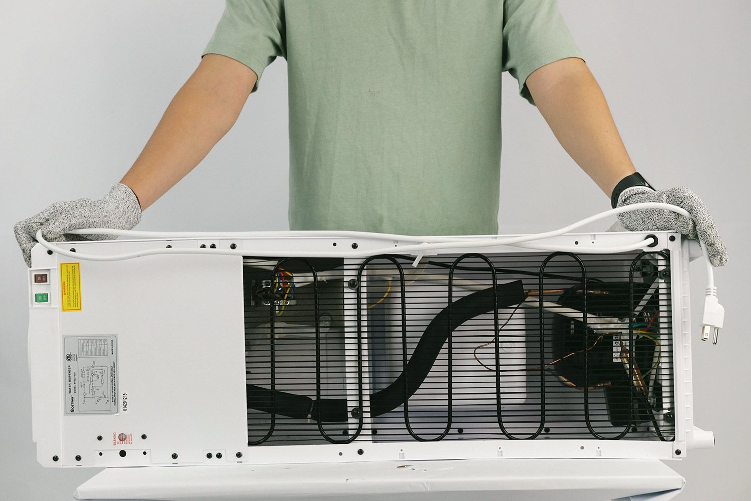 A man holding the electric cord of the Costway 5-gallon water cooler dispenser doubled over the horizontal length of the machine.