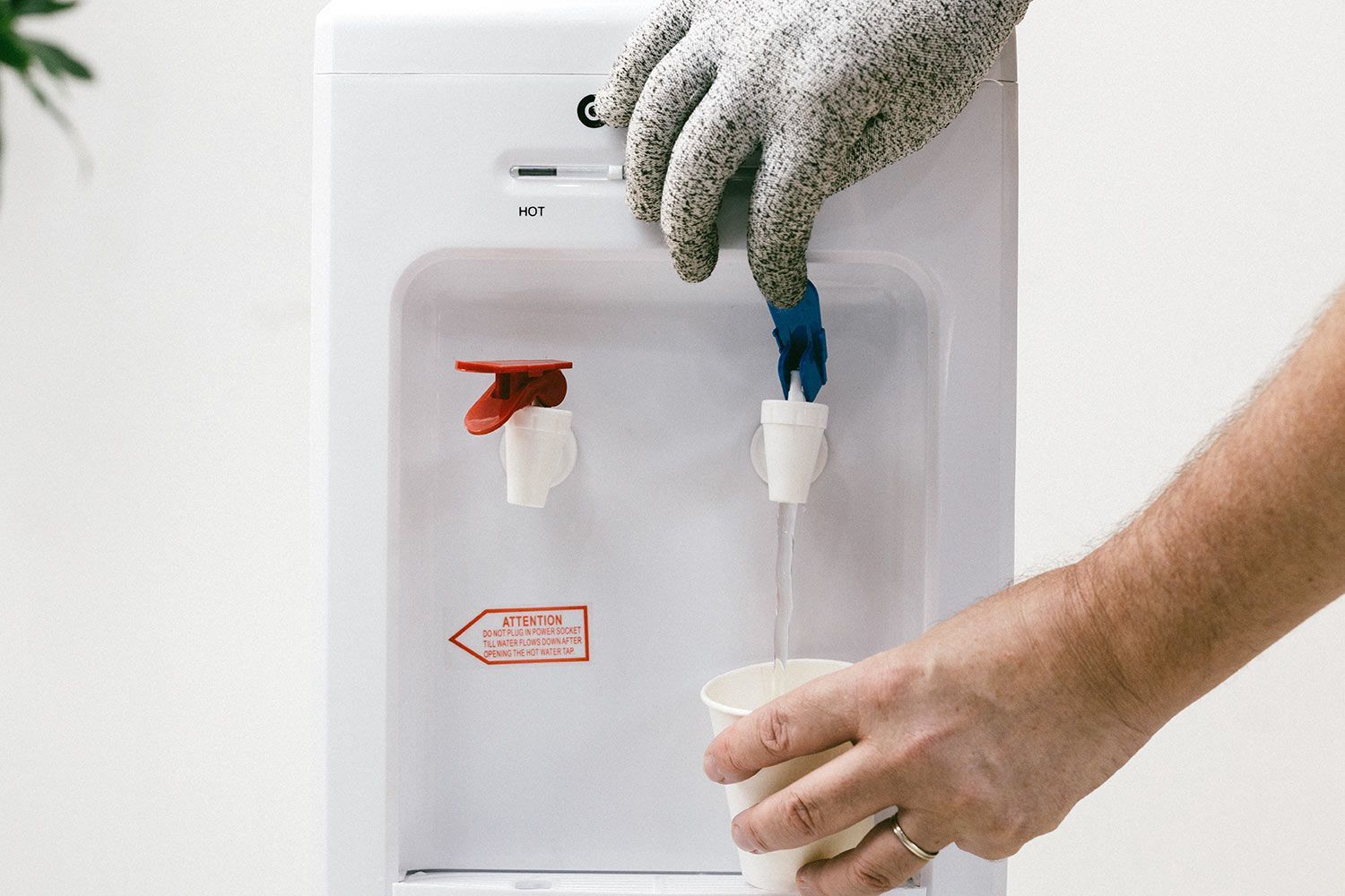 A gloved hand dispensing cold water from the faucet of a water cooler dispenser.