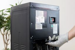 A rear view of a water cooler dispenser and a gloved hand about to lift it gripping the carry handle.