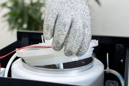 A gloved hand removing lifting up the lid to a cold water tank of a bottom-loading water cooler dispenser.