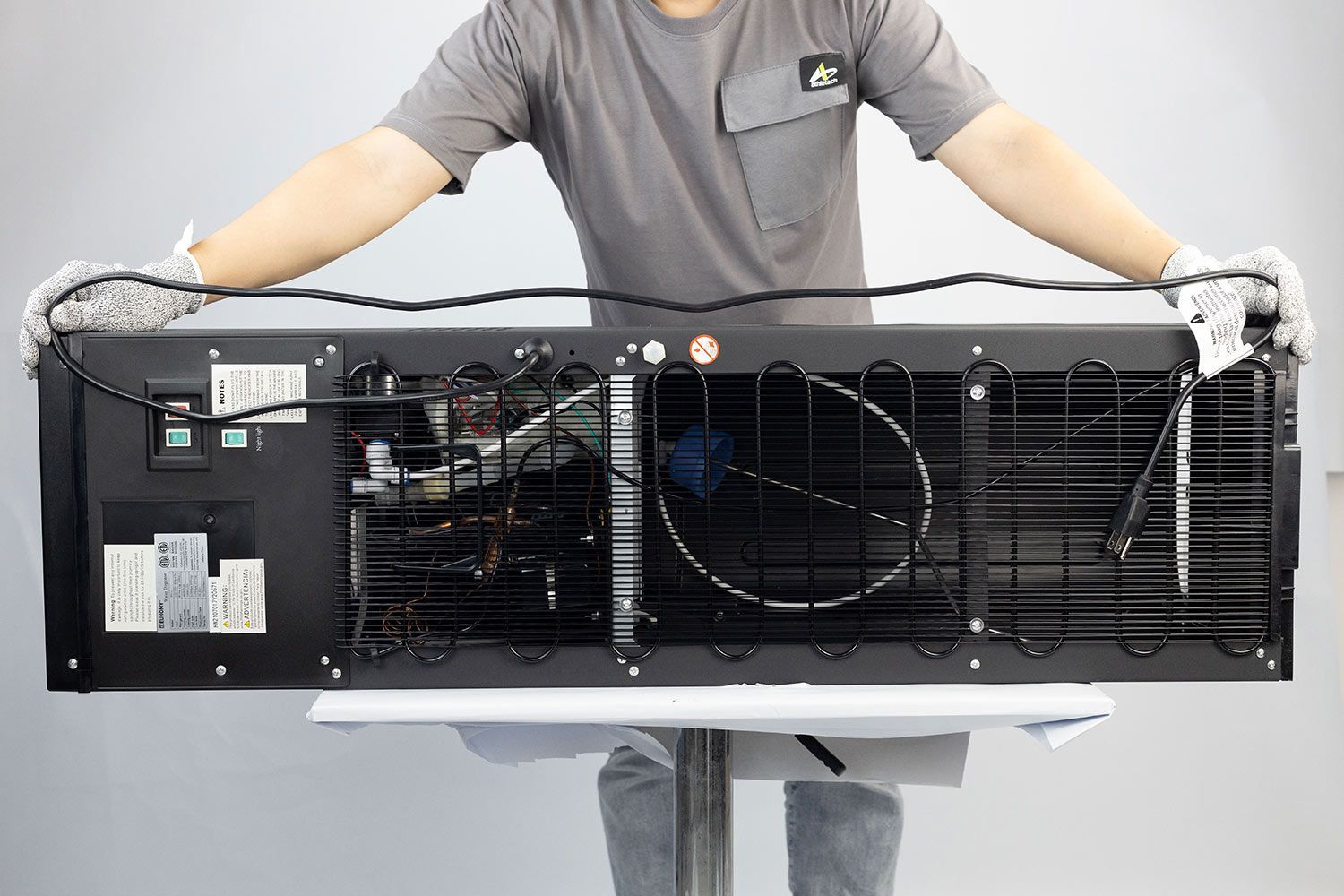 A man holding an electric cord of a water cooler dispenser double-folded across the horizontal length of the machine.