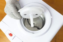 A gloved hand holding a water baffle removed from a cold water tank of a water cooler dispenser. 