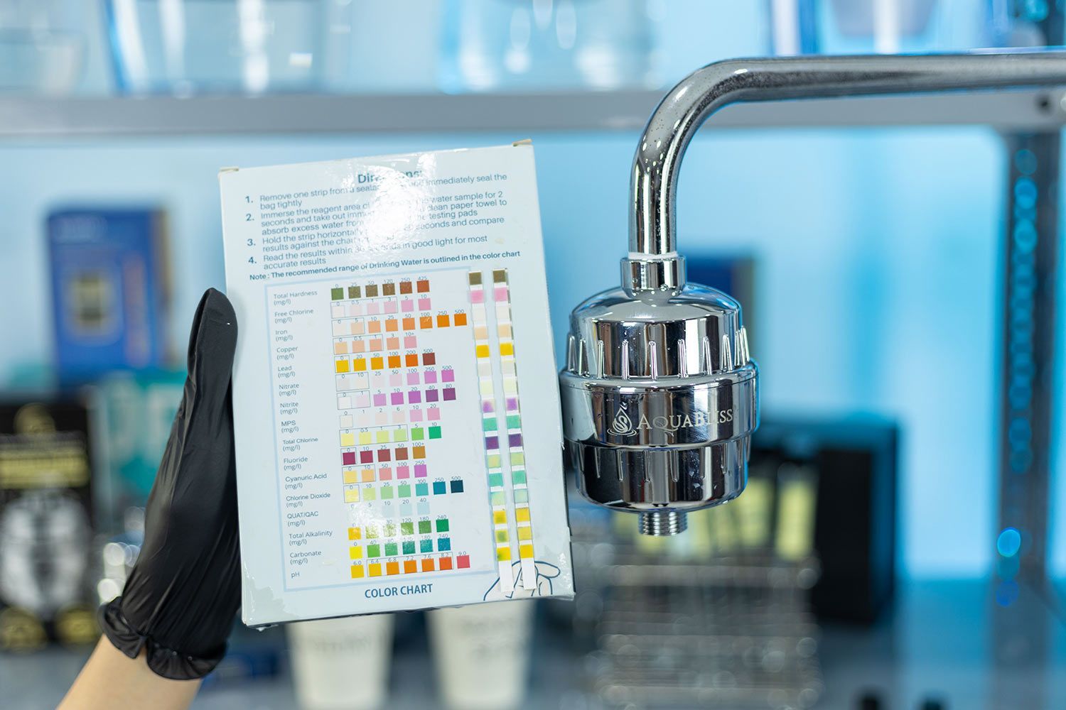 gloved hands holding water test kit box with two used test strips next to Aquabliss shower filter