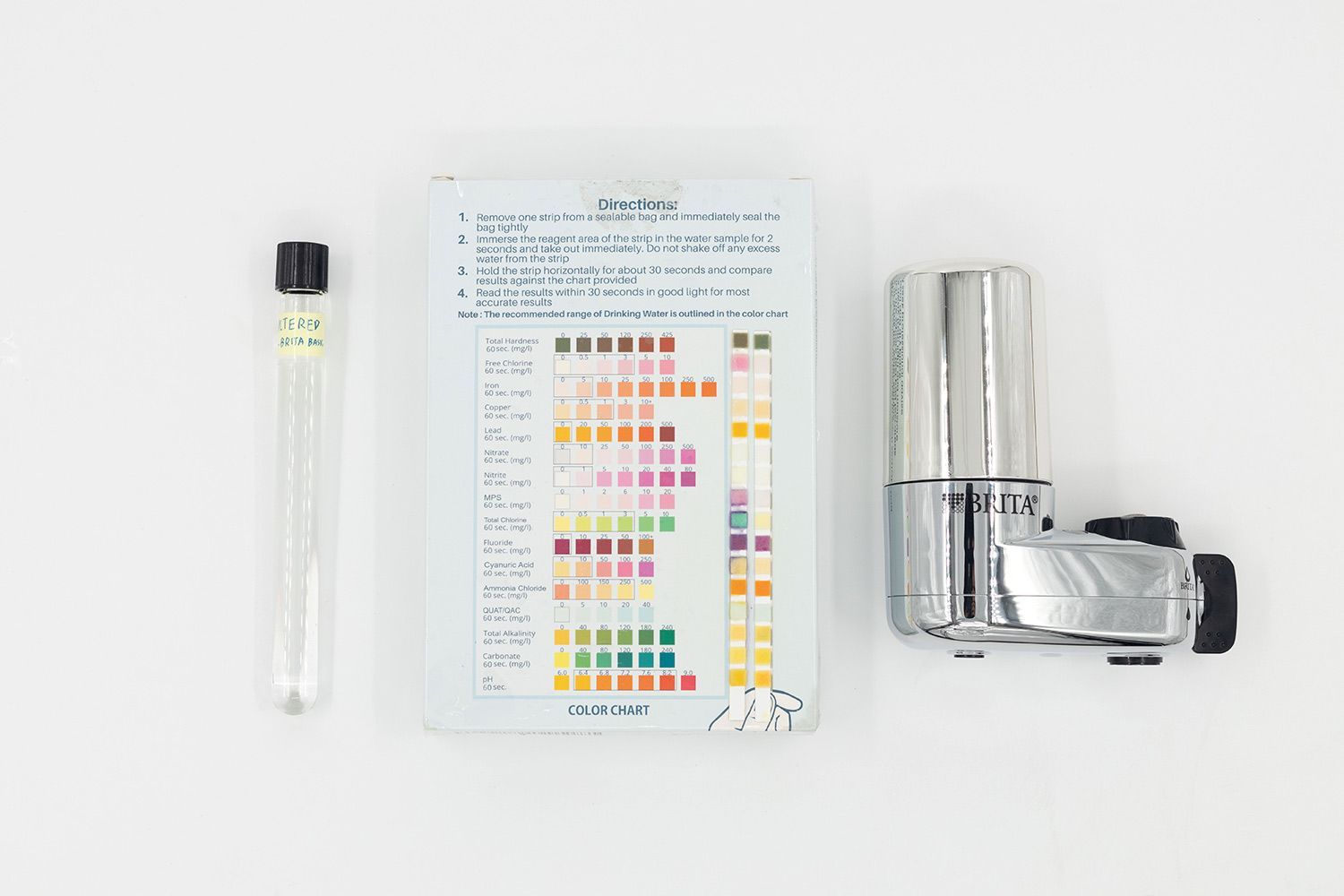 Color chart with used test strips in the center. Vial of sampled water is to the left. Brita Basic filter to the right.