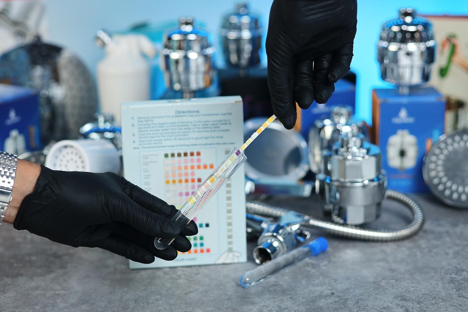 gloved hands holding test tube and test strip, shower filters in background