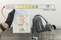 Two water test strips laid on a color chart, held to the left of the PUR Plus FM2500V water filter mounted on a faucet.