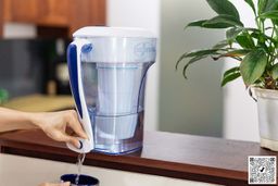 Hand pressing spigot of ZeroWater 10 Cup water filter pitcher to dispense water into cup